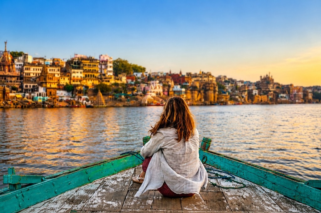 Guest on a wooden boat looking across the Ganges toward the ghats of Varanasi